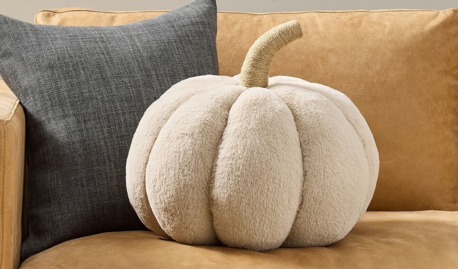 Beige faux for pumpkin shaped pillow sitting on leather couch 