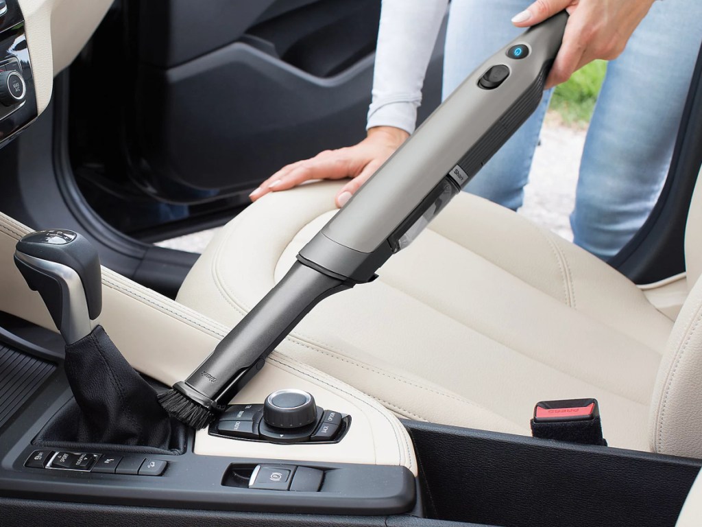 Woman using silver shark wand VAC to clean car