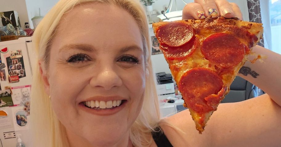 A smiling woman holding a pepperoni pizza slice