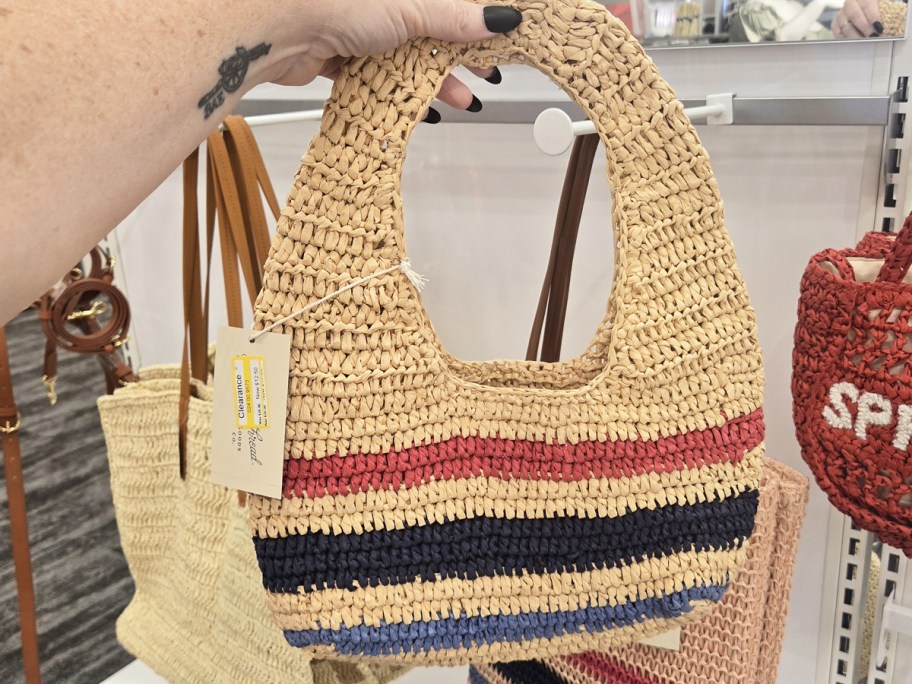 hand holding up a striped straw shoulder bag in store