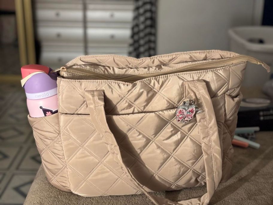 A tan quilted bag with a water bottle on the side
