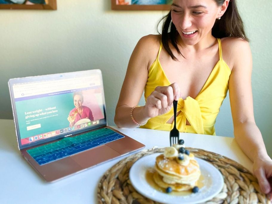 Woman using computer on Weight Watchers website and holding plate of pancakes