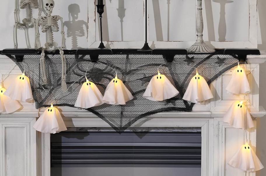 ghost string lights on fireplace mantle with spider webs and skeletons