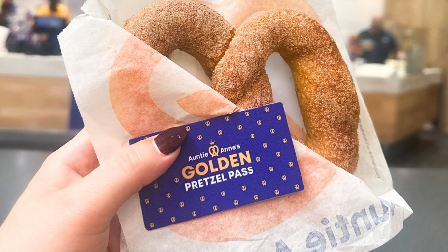 a hand holding a pretzel and a golden pretzel pass card