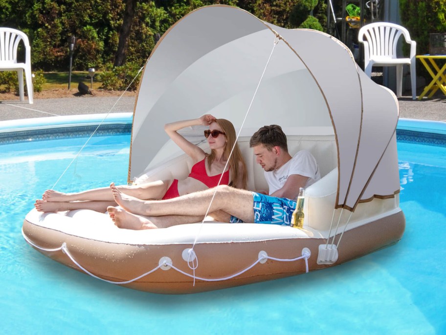two people lounging on a pool float in a pool, with the canopy pulled up