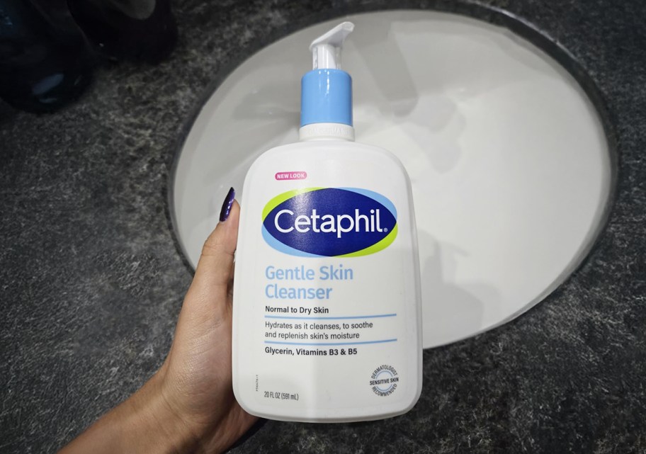 person holding a bottle of cetaphil gentle skin cleanser by a sink