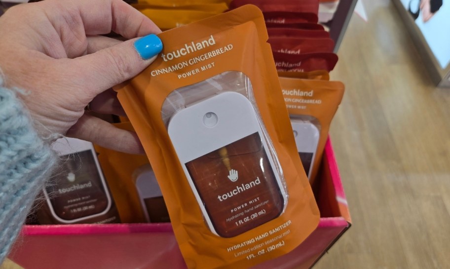 a womans hand holding a packaged touchland hand sanitizer