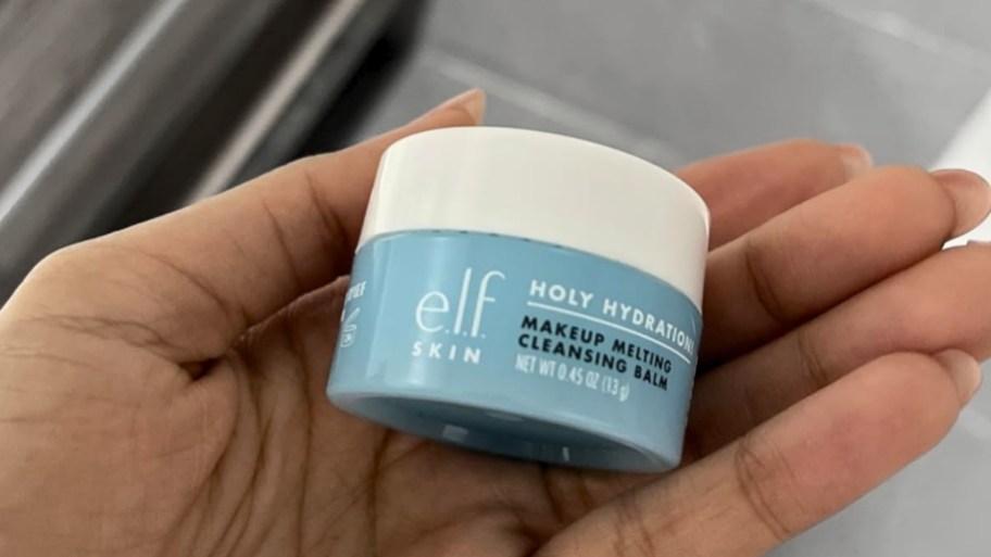 a womans hand holding a mini elf skin cleansing balm
