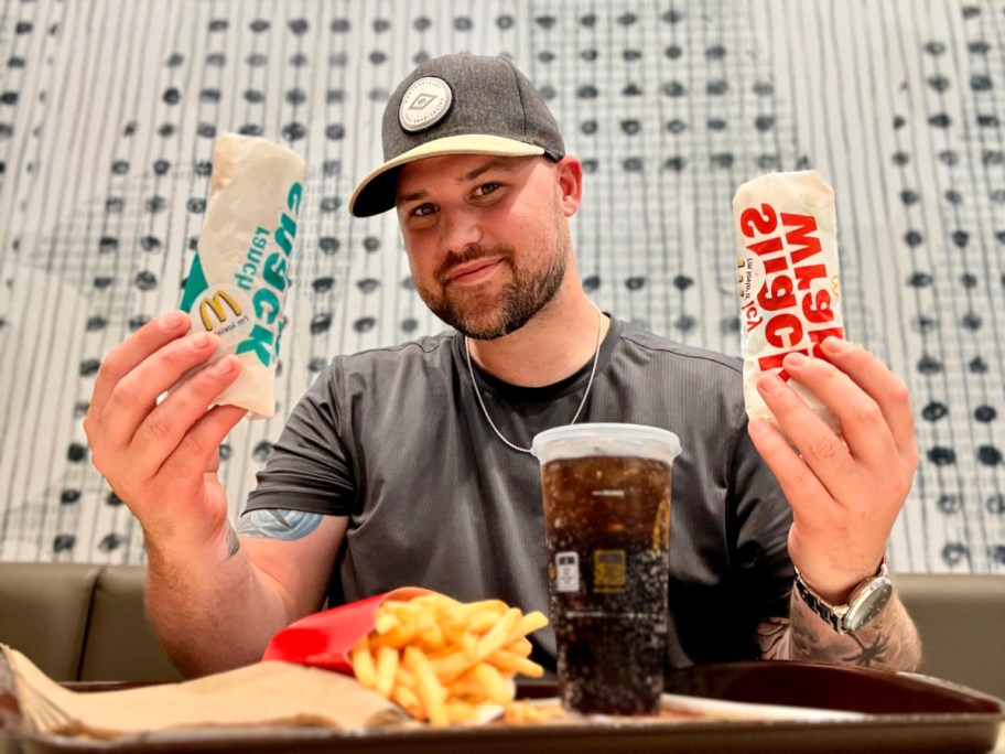 smiling man in a mcdonalds holding up two snack wraps with a tray with a drink and fries