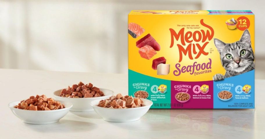 Box of Meow Mix Seafood Favorites featuring a cat, colorful seafood images, and 12 cups label. Three bowls of cat food chunks in gravy sit in front.