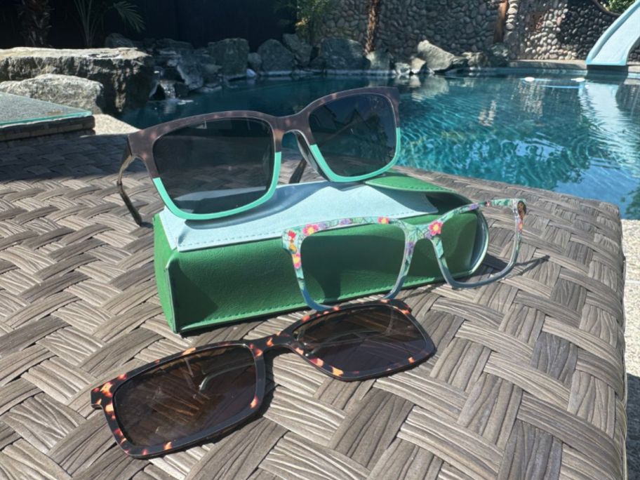 pair of glasses sitting on glasses pouch with 2 toppers laying beside it on table