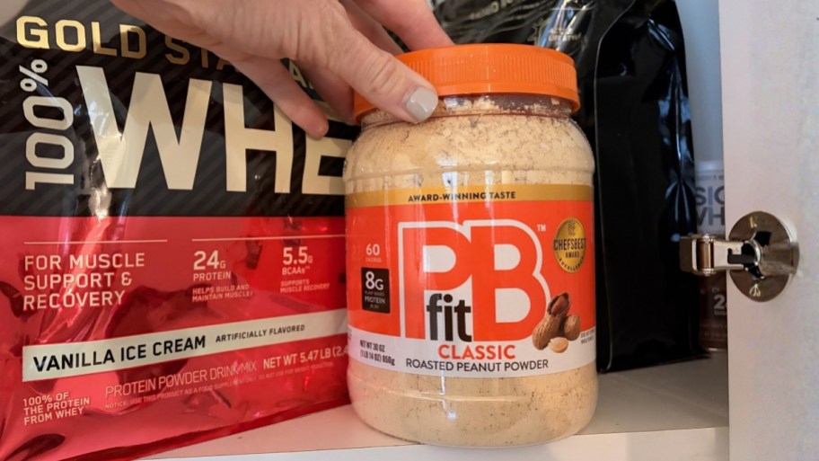 a womans hand reaching for a jar of peanut butter powder