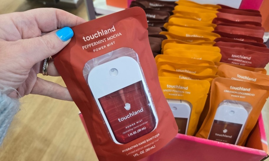 a womans hand holding a packaged touchland hand sanitizer