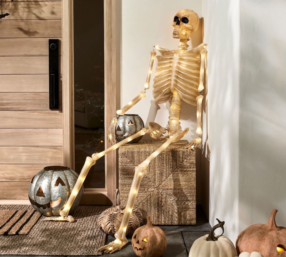 lifesize skeleton with lights sitting on front porch with pumpkins