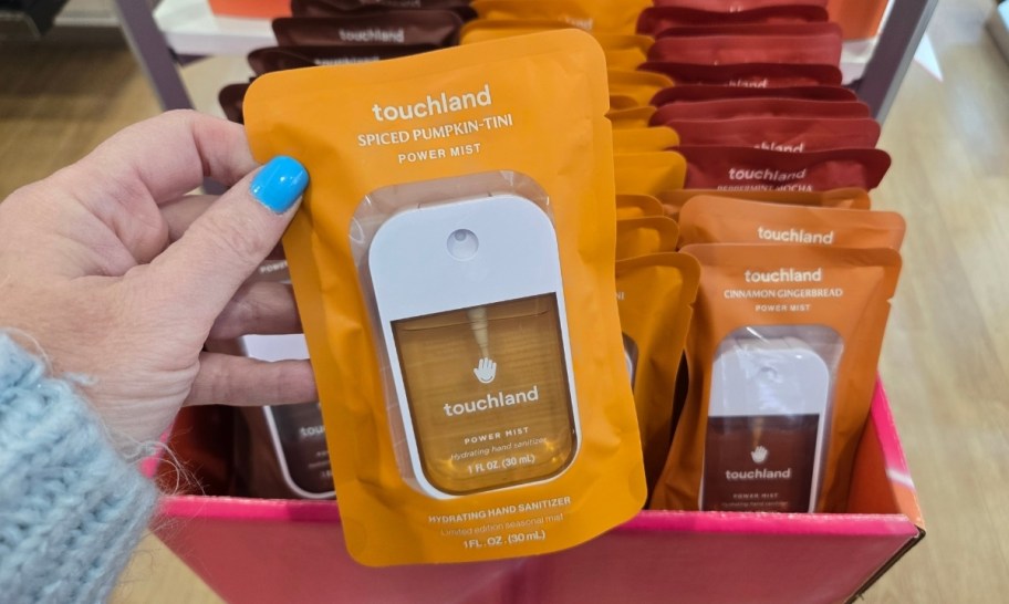 a womans hand holding a packaged touchland hand sanitizer