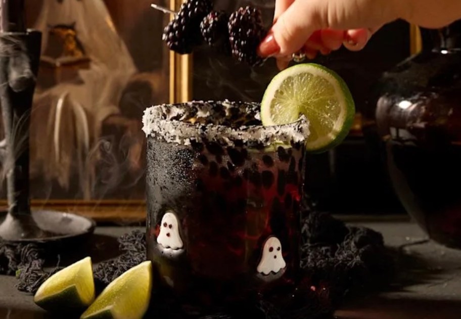 hand putting blackberry garnish on cocktail glass with ghosts