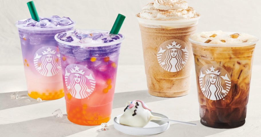 Four colorful Starbucks drinks are displayed: two with purple and orange hues and two iced coffees, alongside a cute unicorn-shaped cake pop on a spoon.