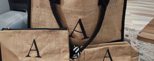 a brown and black tote bag with two makeup bags with an A on them in front of it on table