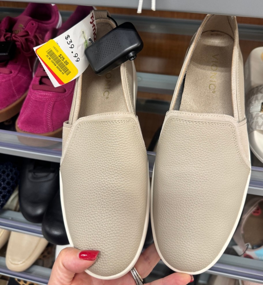 a womans hand holding a pair of tan slip on sneakers