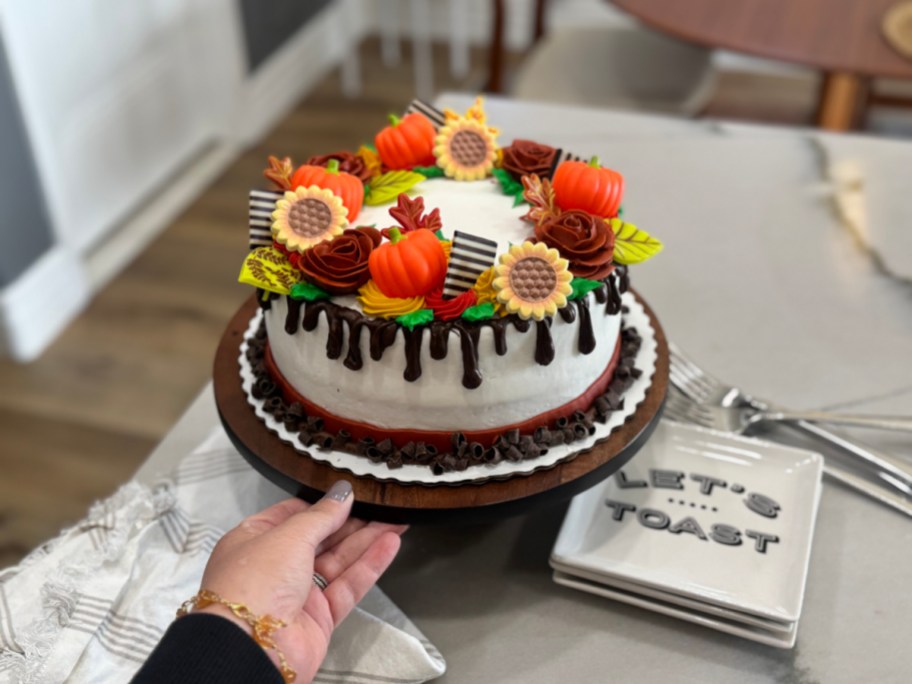 hand lifting the edge of a cake stand with a decorated walmart cake