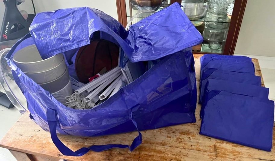 a large blue plastic moving bag filled with items and 5 more folded bags in front