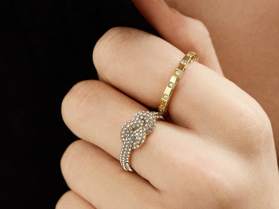 A woman's hand wearing two rings, one in a knot style and the other in a band