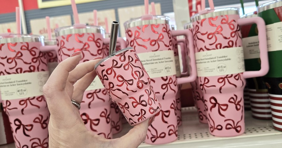 hand holding a mini pink and red bows print tumbler next to larger matching tumblers on store shelf