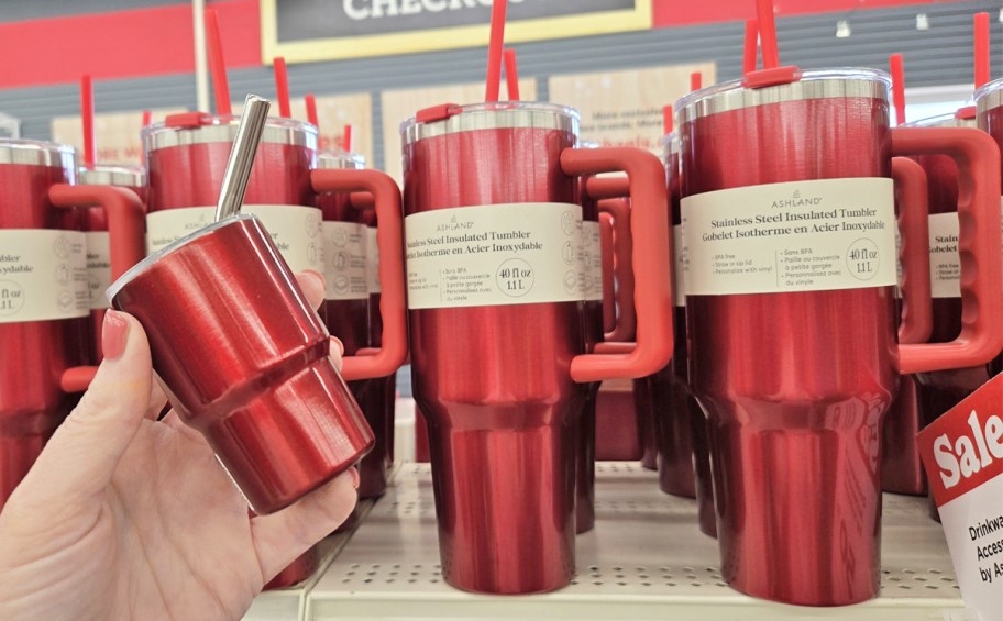 hand holding a mini red tumbler next to larger tumblers on store shelf