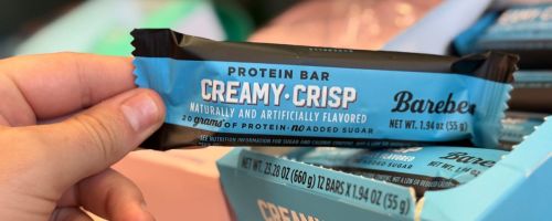 A person holding a Barebells Protein Bar in blue wrapping