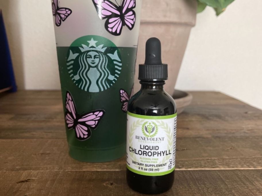A starbucks cup filled with a green liquid next to a bottle of Benevolent Chlorophyll Drops