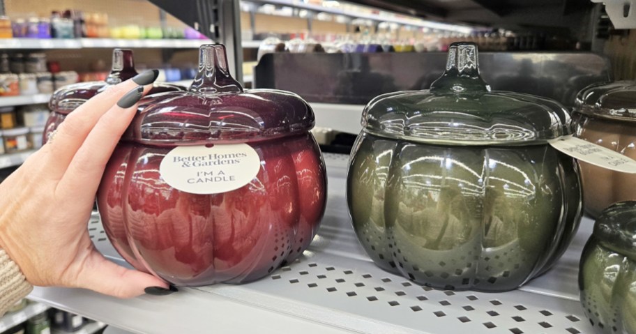 hand touching red and green glass pumpkin jar candles on store shelf
