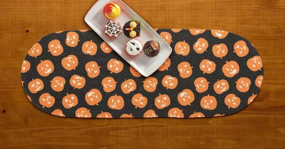 An orange and black Halloween Jack-O'-Lantern Braided Table Runner on a wooden table