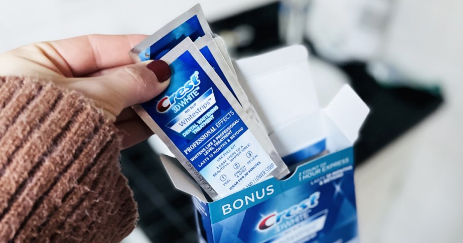 hand grabbing packs of Crest 3D Whitestrips from their box