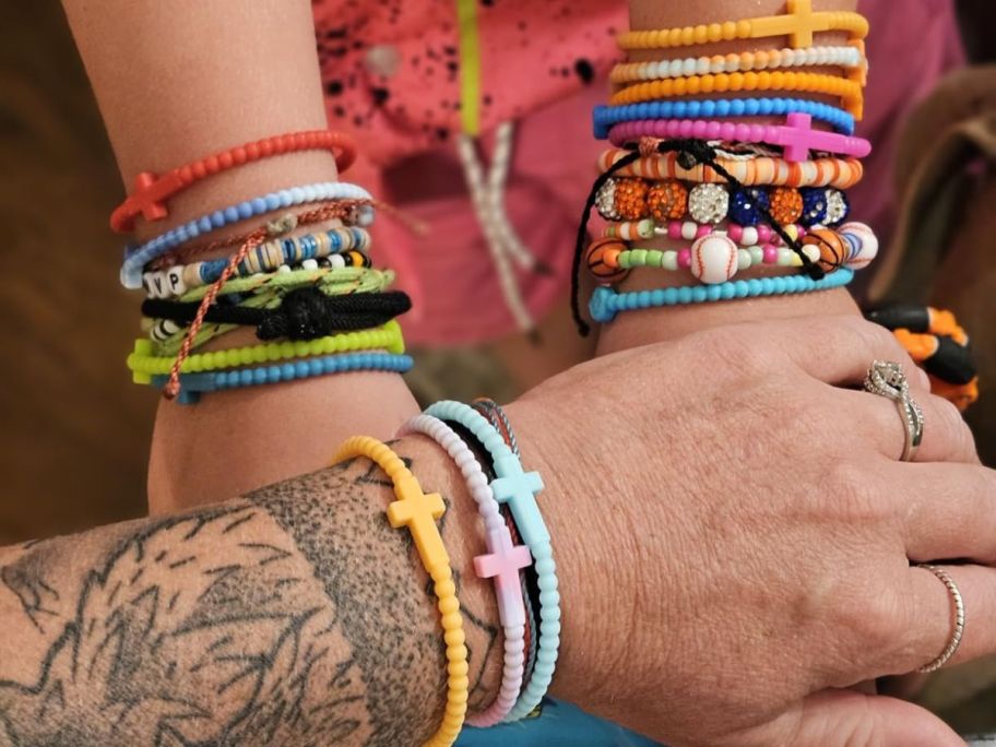 Woman and girl's wrists wearing several bracelets including colorful silicone cross bracelets