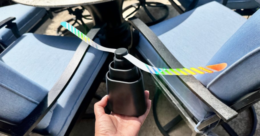 holding a fly fan with holographic strips next to a patio set