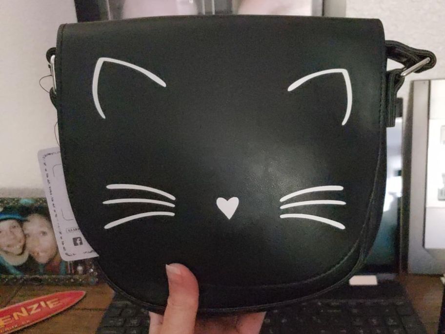 someone holding a black purse with cat ears, nose, and whiskers