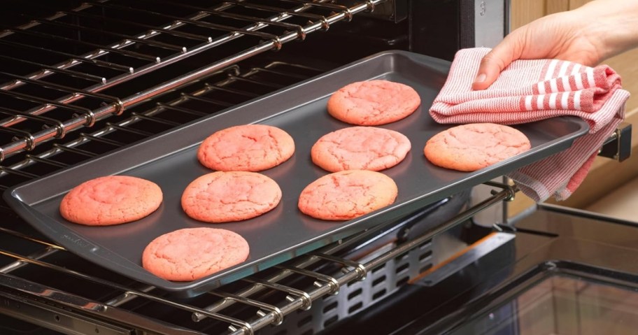 person pulling out cookie sheet filled with pink cookies from the oven