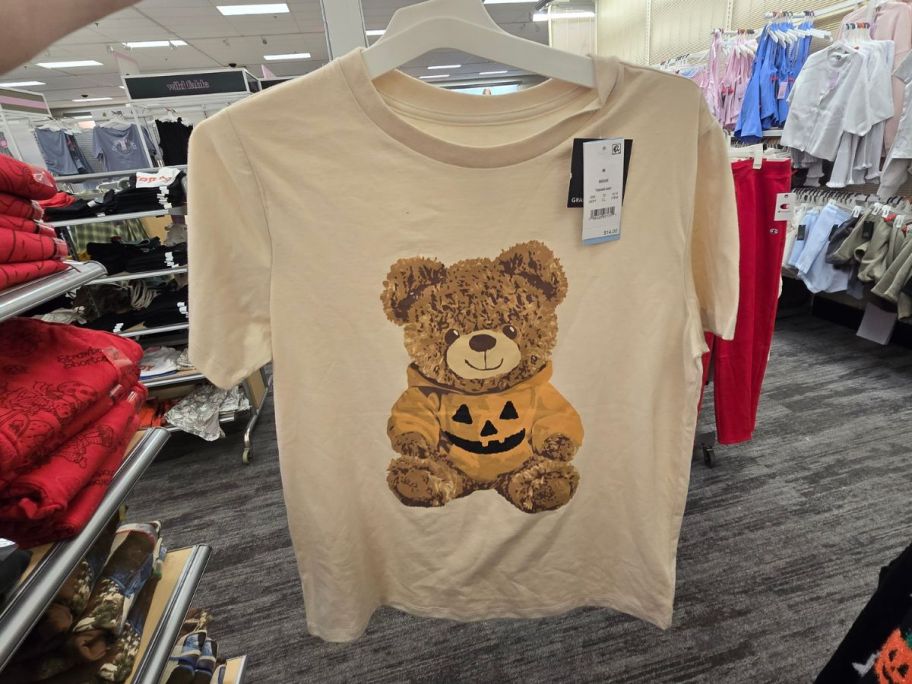A woman holding a t-shirt with a bear clutching a jack o lantern