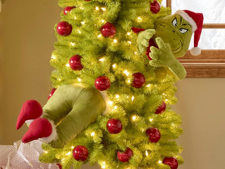 Grinch plush head and legs coming out of decorated Christmas tree