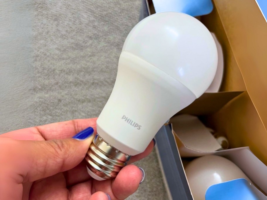 hand holding a Philips light bulb, boxes of more bulbs behind it