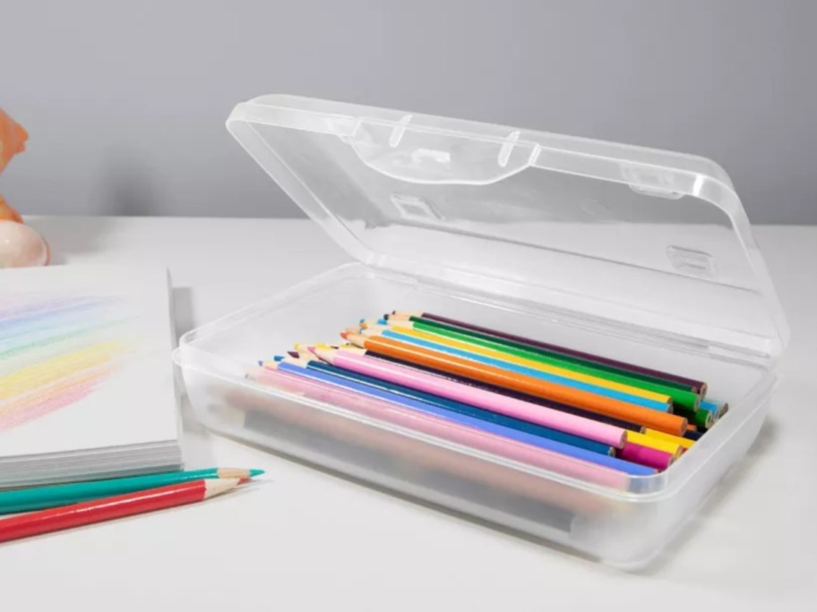 a clear pencil case with colored pencils in it sitting on a desk