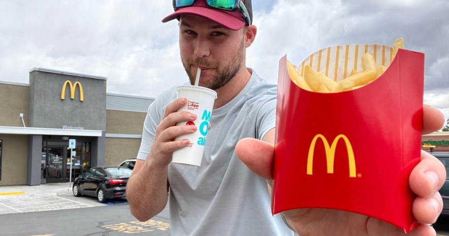 man holding mcdonald's fries and drink in front of restaurant