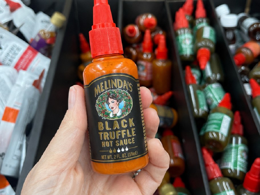 Hand holding mini bottle of Melinda's black truffle sauce inside Walmart store