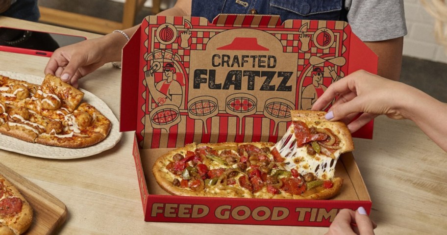 Person grabbing cheesy slice of pizza from Pizza Hut crafted Flatzz box