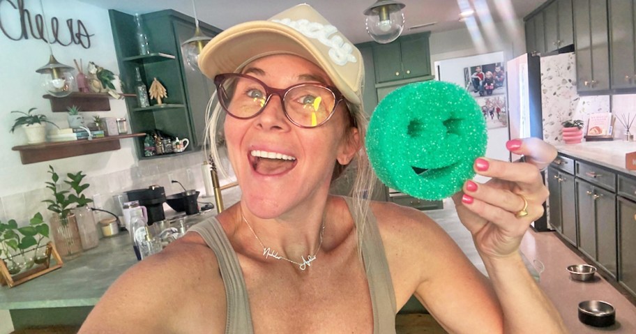 woman holding up a green smiley face sponge 