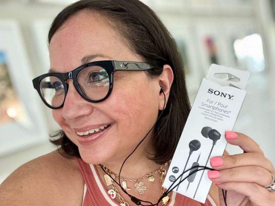 woman wearing Sony Earbuds while holding the box they come in next to her head