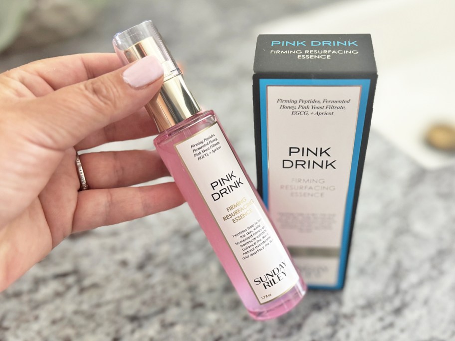 hand holding a bottle of Sunday Riley Pink Drink near bathroom counter