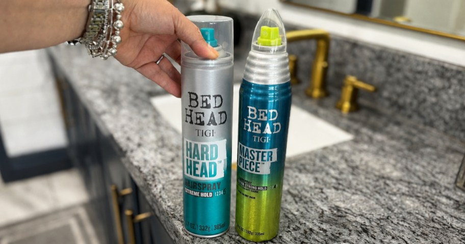 two TIGI Bed Head Sprays on bathroom counter with hand touching one