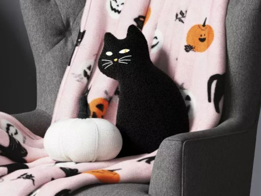 Hyde & Eek! Boutique white pumpkin and black cat halloween throw pillows on a chair with a pink halloween blanket