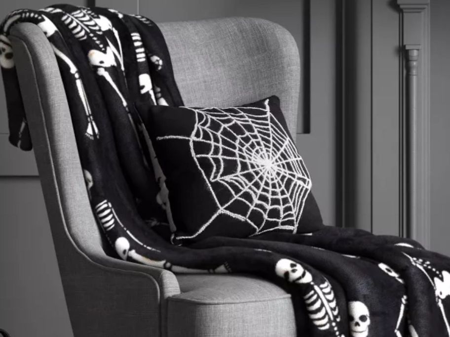 A Hyde & Eek! Boutique Spider Web Throw Pillow on a black skeleton blanket on a chair